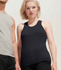 A person with short blonde hair wears the SOLS Ladies Justin Vest, a sleeveless black top with a ribbed neckline, standing beside another in a racerback gray top against a plain light background.