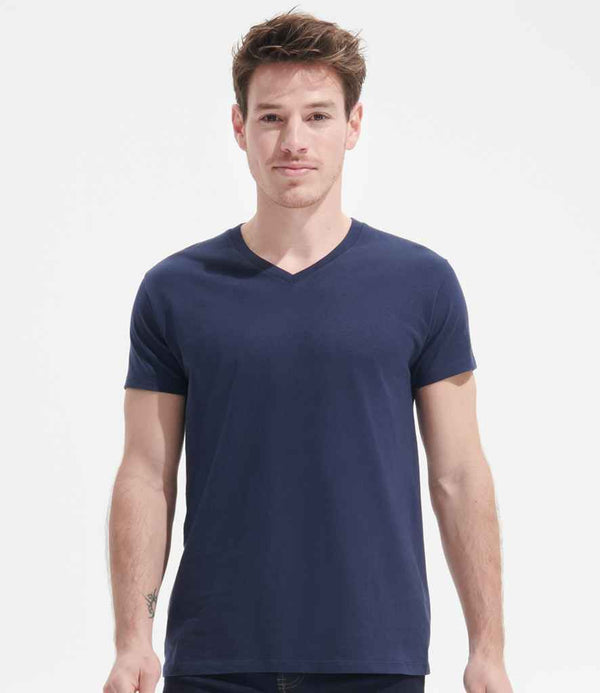 A person with short brown hair stands facing forward, wearing the SOLS Imperial V Neck T-Shirt in navy blue and dark pants against a white background.