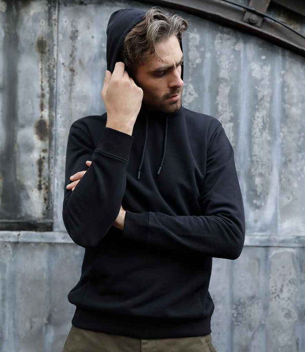 A man stands in front of a corrugated metal wall, looking down and pulling the hood over his head with one hand, wearing the NEOBLU Nicholas French Terry Hoodie by NEOBLU.