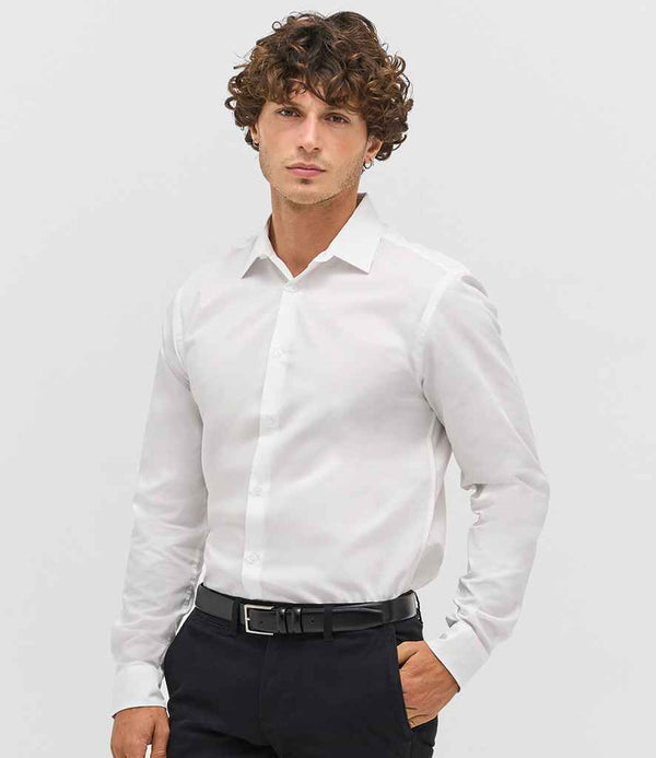 A man with curly brown hair stands against a plain light background, wearing a SOLS Bailey Long Sleeve Poplin Shirt by SOLS, paired with black pants and a black belt. He faces forward with a neutral expression.