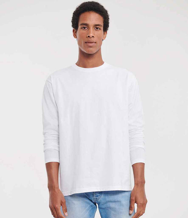 A person faces the camera, wearing a Russell Athletic Classic Long Sleeve T-Shirt in plain white with light blue jeans, set against a simple light background.