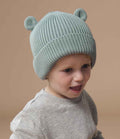 A young child wears a Beechfield Organic Baby Bear Beanie, a light blue ribbed knit hat with 3D ear detail by Beechfield, paired with a light gray sweater, looking slightly to the side against a plain beige background.