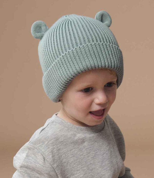 A young child wears a Beechfield Organic Baby Bear Beanie, a light blue ribbed knit hat with 3D ear detail by Beechfield, paired with a light gray sweater, looking slightly to the side against a plain beige background.