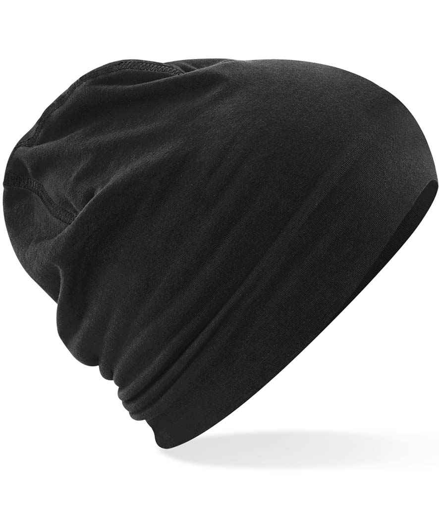 The Beechfield Hemsedal Cotton Beanie by Beechfield is a plain black hat made from soft, lightweight microknit cotton, shown on a white background. It features a slightly slouchy fit and simple overlock stitch detailing along the edges.