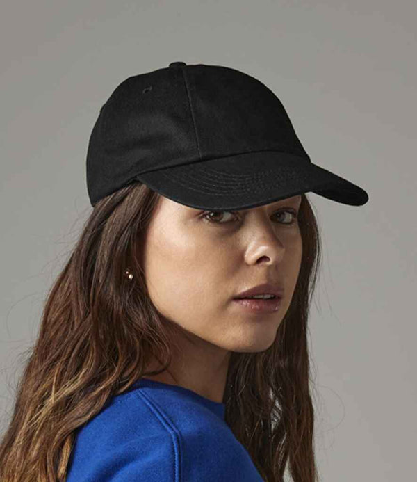 A woman with long brown hair wears a Beechfield Low Profile Heavy Cotton Drill Cap and a blue top, looking over her shoulder at the camera against a neutral background.