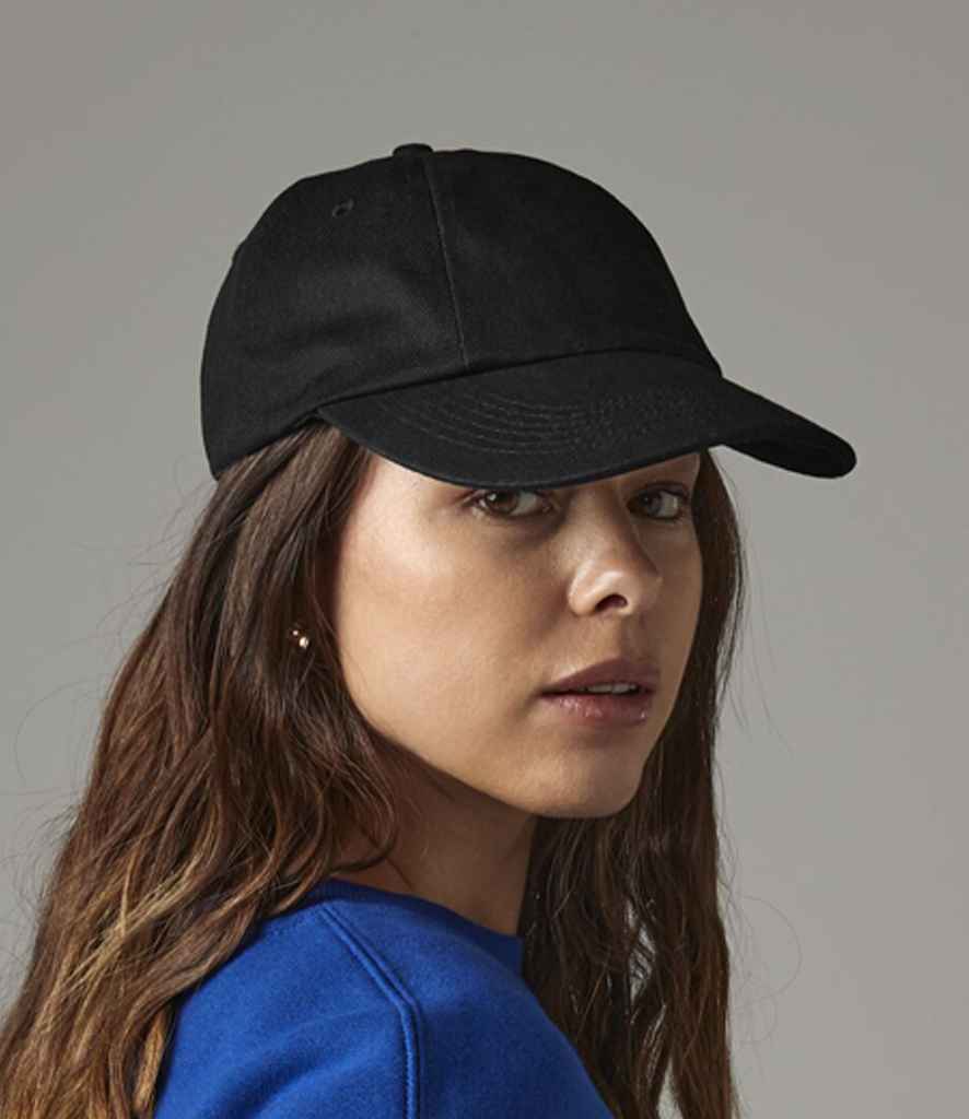 A woman with long brown hair wears a Beechfield Low Profile Heavy Cotton Drill Cap and a blue top, looking over her shoulder at the camera against a neutral background.
