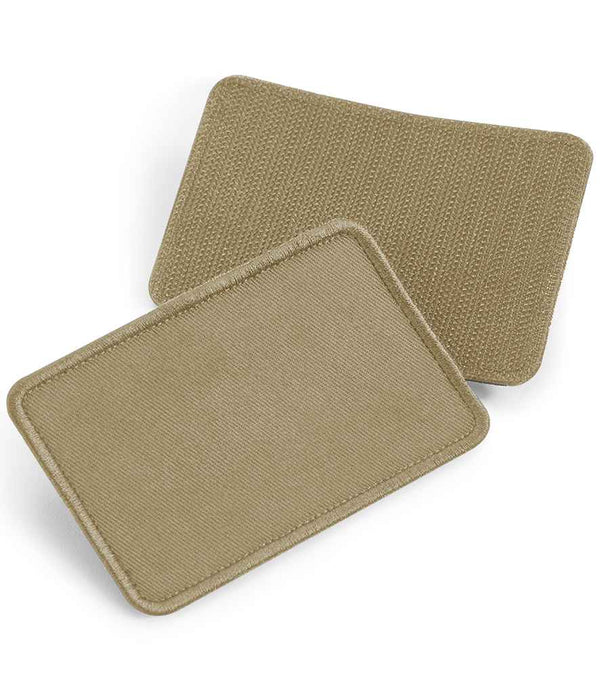 Two rectangular tan Beechfield Removable Cotton Patches are shown, one overlaying the other. The top patch has stitched edges and a smooth surface; the lower one displays the Rip-Strip reverse for easy decoration. Brand: Beechfield.