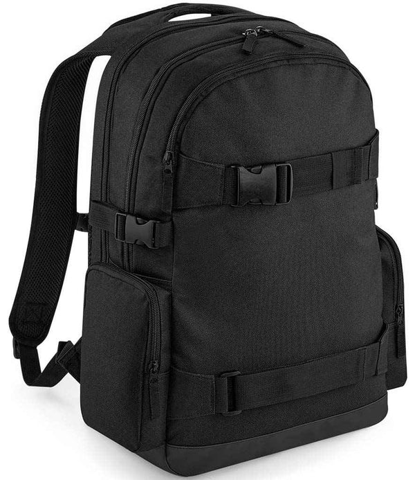 The BagBase Old School Boardpack by BagBase is a black 23L laptop backpack with two main zippered compartments, skateboard carry straps, side pockets, adjustable shoulder straps, and buckle closures, shown on a plain white background.