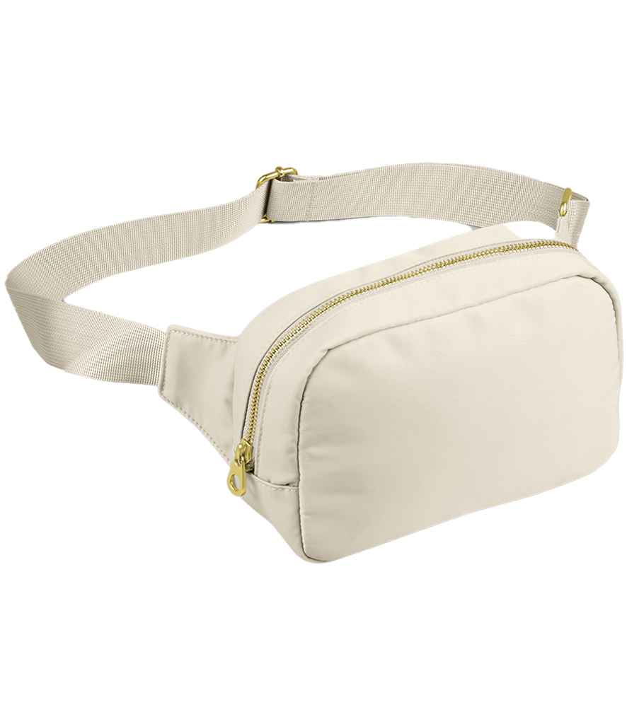 The BagBase Sundae Cross Body Bag by BagBase is a beige fanny pack with premium fabric, a zippered main compartment, adjustable webbing strap, and gold-tone zipper hardware, shown on a white background.