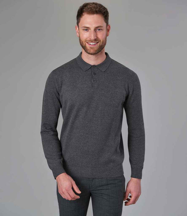 A man with short hair and a beard stands smiling in the Brook Taverner Casper Knitted Long Sleeve Polo Shirt, featuring a pique collar and button placket, paired with dark pants against a plain gray background.