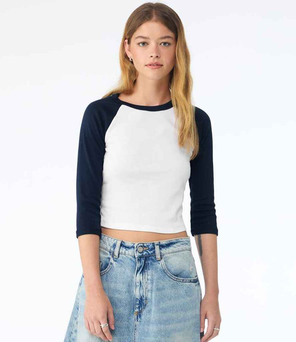 A woman with long light brown hair is wearing the Bella+Canvas Bella Ladies Micro Rib 3/4 Raglan Baby T-Shirt and a light blue denim skirt, standing against a plain light background.