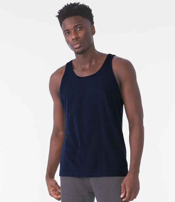 A man models the Bella+Canvas Canvas Unisex Jersey Tank Top in dark blue with a bound neckline and gray pants, standing against a white background and looking directly at the camera with a neutral expression.