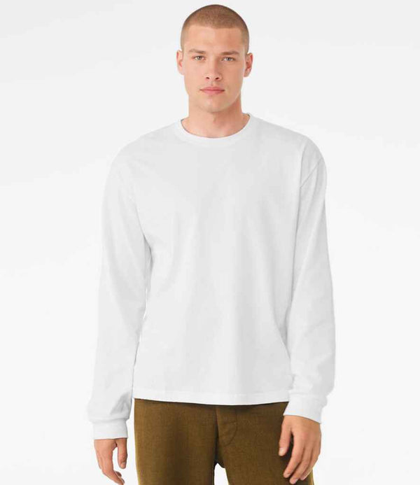 A person with short hair stands facing forward against a white background, wearing brown pants and a Bella+Canvas Canvas Unisex Heavyweight Long Sleeve Boxy T-Shirt in white, featuring a ribbed collar.