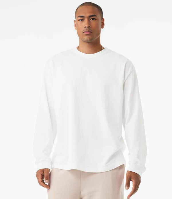 A person stands facing forward against a white background, wearing the Bella+Canvas Canvas Unisex Heavyweight Long Sleeve T-Shirt in plain white and light beige pants.