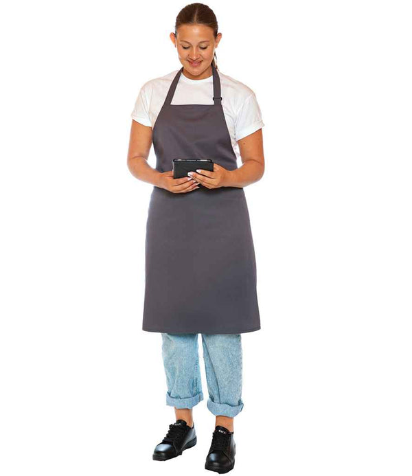 A person wearing a white t-shirt, Dennys Polyester Bib Apron by Dennys in gray, light blue jeans, and black shoes stands holding a digital tablet and looks down at the screen against a white background.