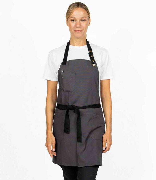 A person faces forward against a plain white background, wearing a white t-shirt and the Dennys Canvas Apron with Front Split by Dennys, featuring an adjustable stud neckband, front pocket, and black webbing ties.
