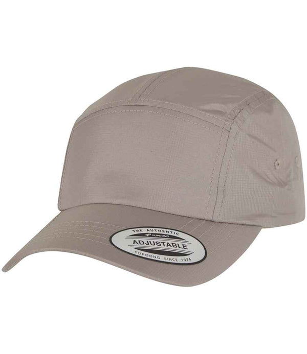 The Flexfit Jockey Elastic Cap by Flexfit features a light brown structured front panel, pre-curved peak, and adjustable back strap. A sticker on the brim reads Adjustable with additional product details.