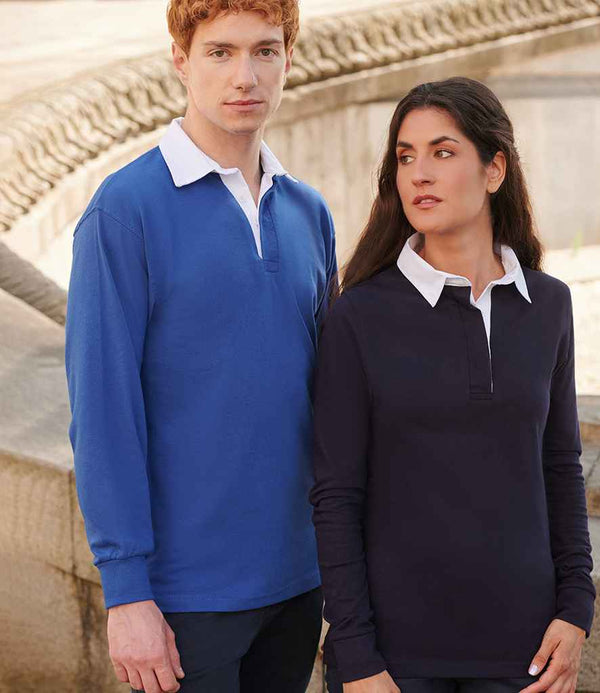 A man wears a blue Front Row Classic Rugby Shirt with a woven collar, while a woman sports the same shirt in black with a white collar. Both enjoy leisure time outdoors near stonework, showcasing their stylish Front Row attire.