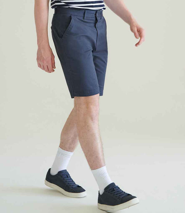 A person wears Front Row Stretch Chino Shorts in dark blue with a YKK zip fly, paired with a striped shirt, white socks, and navy sneakers, standing against a plain light background. The image is cropped at the shoulders.
