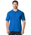 A man faces forward wearing the Gildan Hammer Piqué Polo Shirt by Gildan in bright blue, featuring a ribbed collar and three-button placket, paired with dark pants against a white background.
