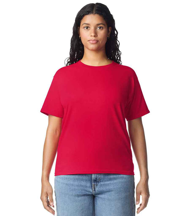 A person with long, dark hair stands facing forward, wearing a Gildan Ladies Heavy Cotton™ T-Shirt in red by Gildan and light blue jeans against a white background.