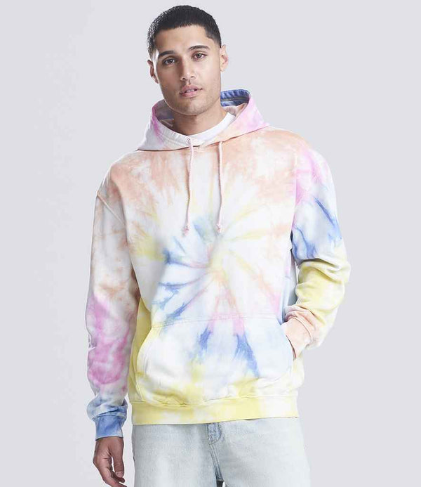 A man faces forward in a pastel AWDis Tie-Dye Hoodie by Just Hoods, featuring yellow, blue, pink, and white brushed back fleece. His right hand is in the front pouch pocket. He pairs the hoodie with light jeans against a light gray background.