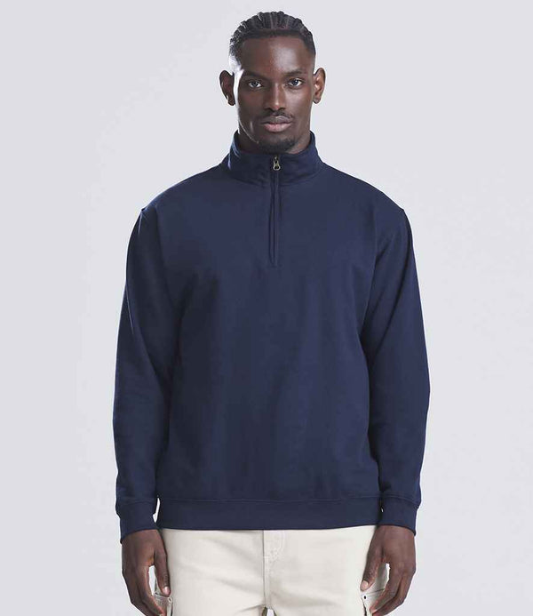 A man faces forward in a Just Hoods AWDis Sophomore Zip Neck Sweatshirt, navy blue with a YKK zip, paired with light pants against a plain light gray background.