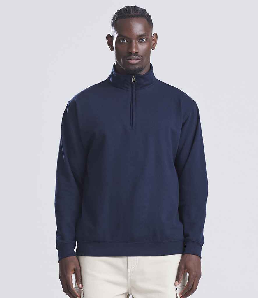 A man faces forward in a Just Hoods AWDis Sophomore Zip Neck Sweatshirt, navy blue with a YKK zip, paired with light pants against a plain light gray background.