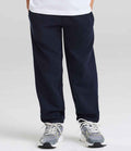 A person wears Just Hoods AWDis Kids Cuffed Jog Pants in navy blue with gray sneakers, standing against a plain light background. Only the lower half of the body is visible.