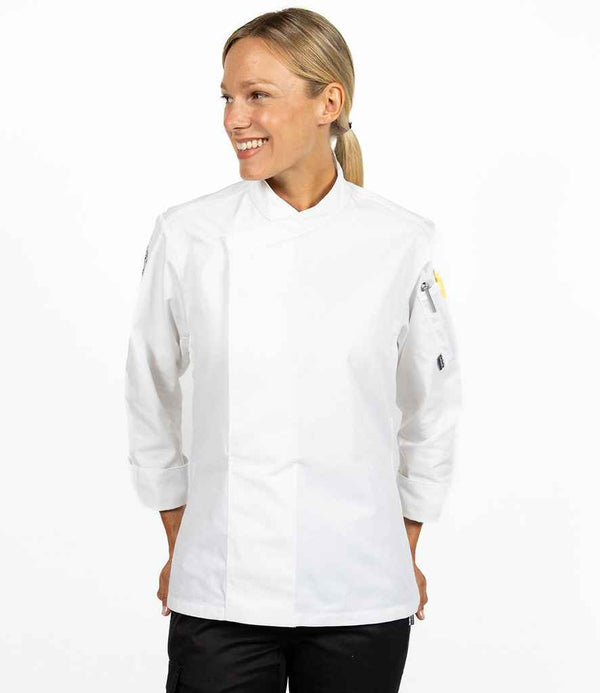 A woman with blonde hair tied back wears the Le Chef Long Sleeve Academy Tunic by Le Chef and black pants, standing against a white background and smiling while looking to her left.