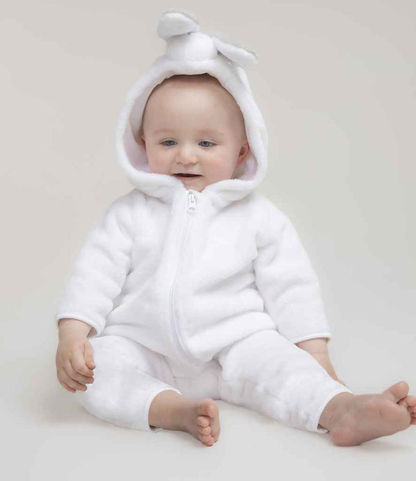 A baby sits barefoot on a light surface, wearing the Larkwood Baby/Toddler Rabbit All In One by Larkwood—a white hooded onesie with small rabbit ears, a longline YKK zip, and no tags—looking forward with a slight smile.