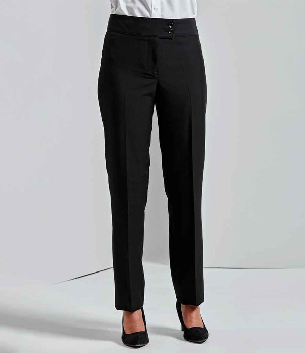 A person wears Premier Ladies Iris Straight Leg Trousers by Premier with a white button-up shirt and black closed-toe heels, standing against a plain light background. The photo is cropped at the shoulders.