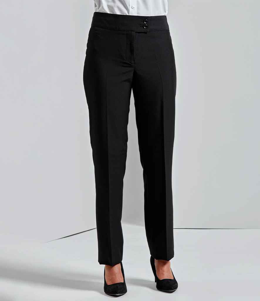 A person wears Premier Ladies Iris Straight Leg Trousers by Premier with a white button-up shirt and black closed-toe heels, standing against a plain light background. The photo is cropped at the shoulders.