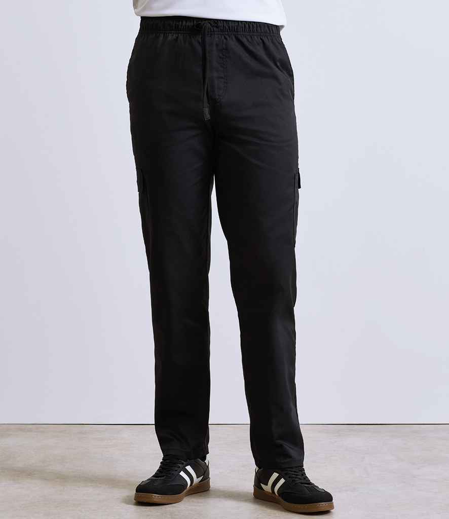 A person is wearing Premier Essential Chefs Cargo Trousers by Premier, featuring cargo pockets, an elasticated waistband, and a relaxed fit, paired with black sneakers with white stripes, standing indoors against a plain light background.