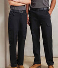 Two people stand side by side, each wearing Premier Unisex Stretchchecker Work Cargo Trousers with black belts, gray shirts, and tan work boots. Their upper bodies are partly out of frame against a plain, light-colored background.