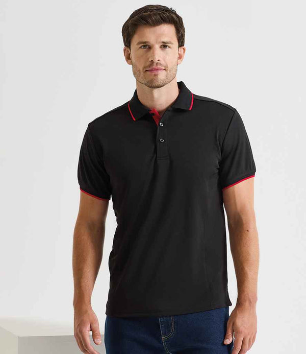 A man is wearing the Premier Contrast Coolchecker® Piqué Polo Shirt by Premier, featuring a ribbed collar with red trim on the sleeves, paired with blue jeans. He stands facing forward and looks at the camera against a plain background.