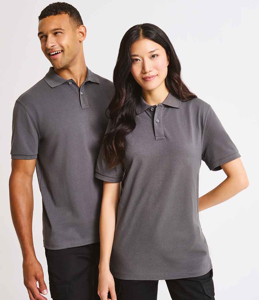 Two people wear matching Premier Essential Unisex Polo Shirts by Premier, featuring short sleeves and a ribbed collar, standing side by side against a plain background. One smiles and looks away; the other faces forward with a neutral expression.