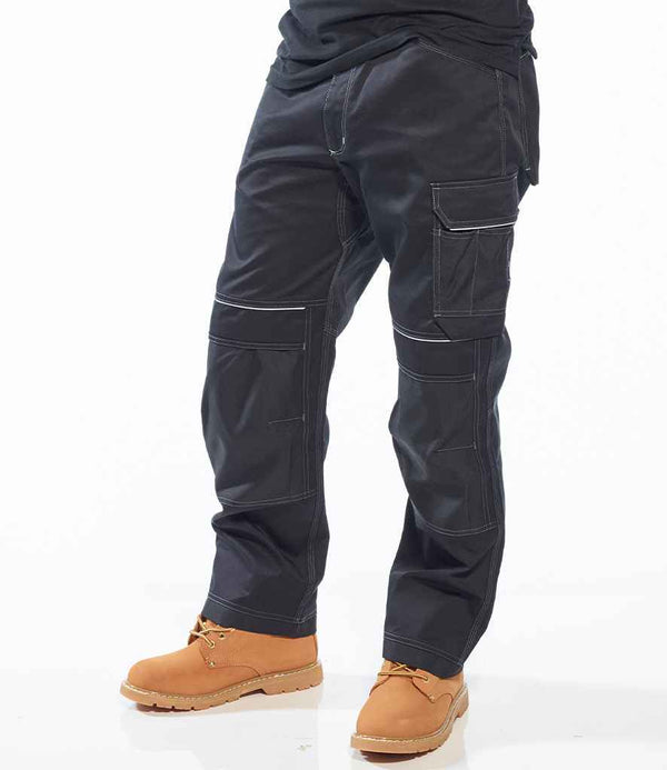 A person wearing Portwest PW3 Work Trousers with multiple pockets and tan work boots stands against a plain white background, showing only the lower half of the body.
