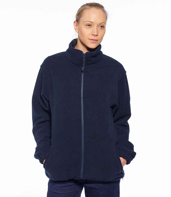 A person stands facing forward with hands in the pockets of a dark navy Portwest Argyll Heavy Fleece Jacket by Portwest, featuring a full-length zip, against a plain white background.