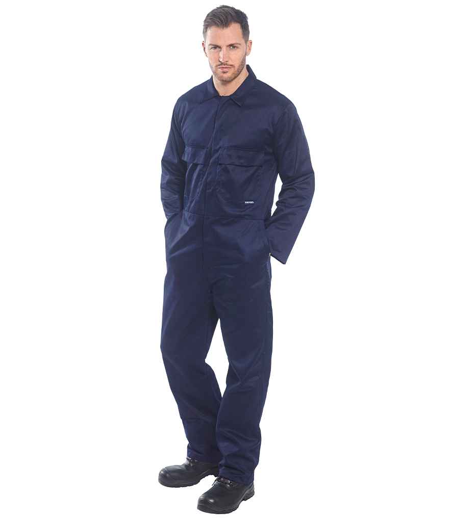 A man stands facing forward against a plain white background, wearing the Portwest Euro Work Coverall in dark blue with chest pockets and an elasticated waistband from Portwest, paired with black work boots and hands in his pockets.