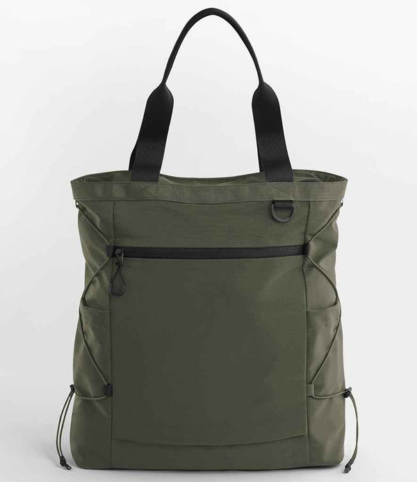 The Quadra UrbanShift Tote Bag by Quadra is green with black handles, a front zippered pocket, side drawstrings for bungee compression, and a D-ring on the upper front, shown against a plain white background.