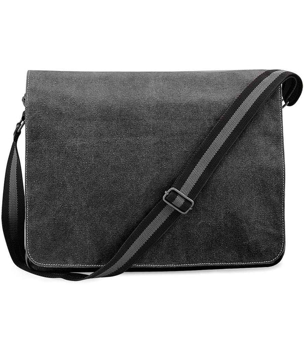 The Quadra Vintage Canvas Despatch Bag by Quadra features dark gray canvas, a flap closure, an adjustable black strap with a white center stripe, visible edge stitching, and zip compartments for secure storage.