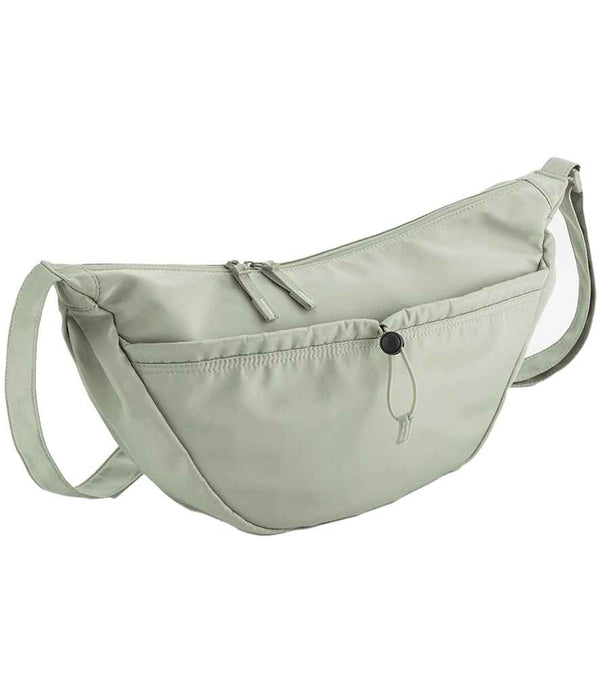 The Quadra Studio Cross Body Bag by Quadra is a light sage green bag featuring an adjustable strap, main zip compartment, and large front pocket with button closure—a minimalist design ideal for everyday essentials.