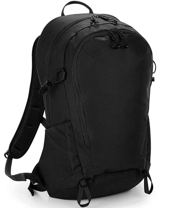 The Quadra SLX-Lite 25 Litre Daypack from Quadra is a black backpack with a streamlined design, two zippered compartments, adjustable shoulder straps, top handle, bottom attachment loops, and hydration bladder compatibility. Photographed upright on white.