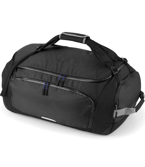 The Quadra SLX 60 Litre Haul Bag by Quadra is a black, water repellent duffel bag with two zippered front pockets, black handles with gray grip, an adjustable shoulder strap, and side handles, shown here on a white background.