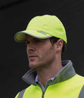 A man with short hair stands against a dark background, wearing a Result Headwear Result High-Viz Cap and a matching safety vest. He looks slightly to the side.