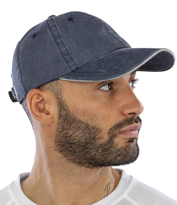 A man with a trimmed beard and mustache wears the Result Washed Fine Line Cotton Cap by Result Headwear in dark blue, paired with a white shirt, looking right against a plain white background.