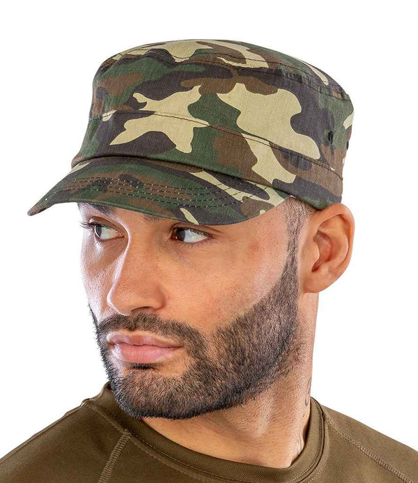 A man with a trimmed beard wears the Result Urban Camo Cap by Result Headwear, featuring stitched eyelets, along with an olive green shirt as he looks to his left against a plain white background.