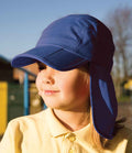 A child wearing the Result Kids Fold Up Legionnaires Cap by Result Headwear and a yellow polo stands outdoors in sunlight with eyes closed, looking slightly to the side; background is blurred.