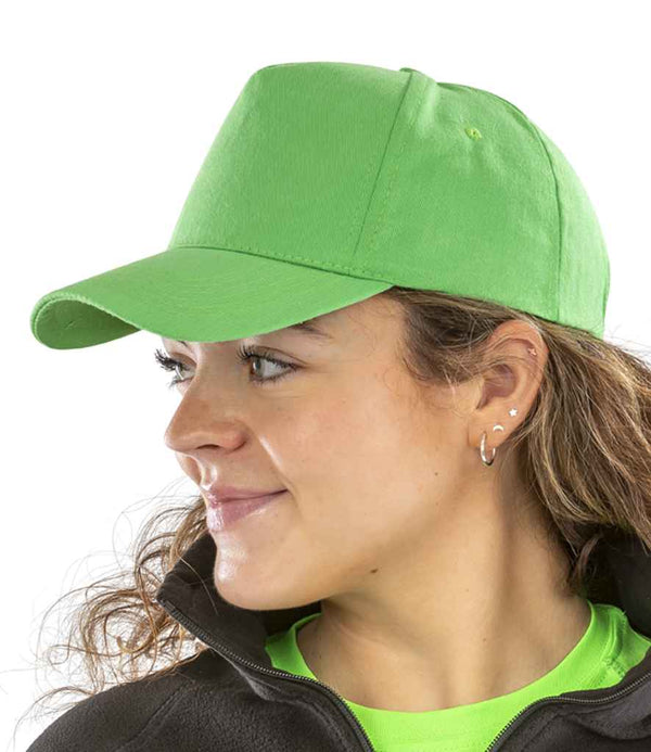 A person with curly brown hair, hoop earrings, and multiple ear piercings is shown in profile facing left. They wear a bright green Result Boston 5 Panel Printers Cap by Result Headwear, a green shirt, and black jacket against a white background.